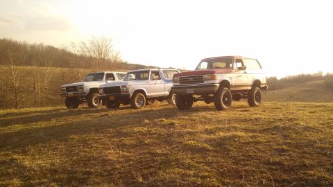 1979 Ford Bronco - Three SUVs are parked on a grassy hill during golden hour.