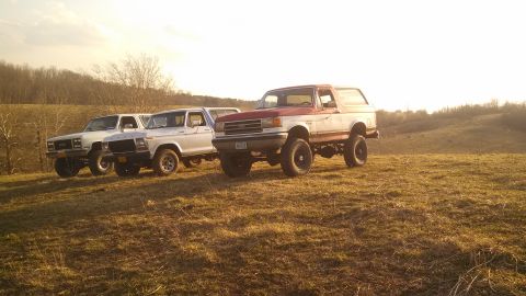 1979 Ford Bronco - Three SUVs parked on a grassy hill during sunset. The lead vehicle is a red and white Ford Bronco.