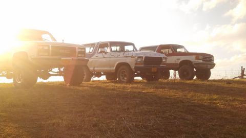 1979 Ford Bronco - Three off-road vehicles are parked on a hill during a golden hour sunset.