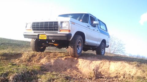 1979 Ford Bronco - This Ford Bronco is navigating a challenging dirt incline under a clear blue sky.