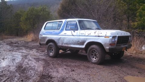 1979 Ford Bronco - A white and blue Ford Bronco is driving on a muddy, wooded trail.