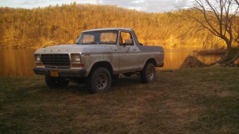 1979 Ford Bronco - A weathered tan Ford Bronco sits by the water's edge as the sun sets, casting a warm glow on the landscape.