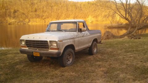 1979 Ford Bronco - A 1979 Ford Bronco sits parked on a grassy bank next to a calm river, bathed in the warm light of sunset.
