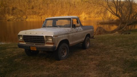 1979 Ford Bronco - Ford Bronco parked near water with trees in the background.
