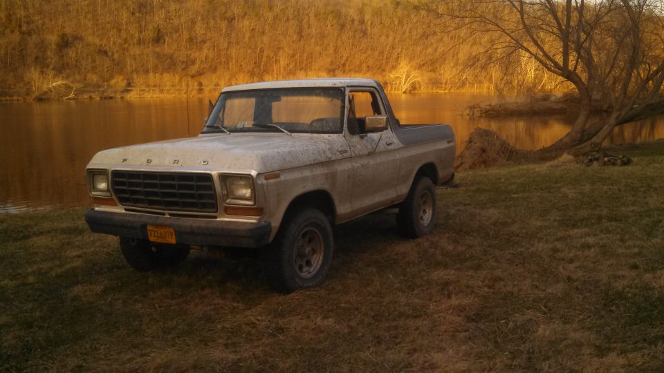 1978 Ford Bronco parked on grassy bank next to a body of water