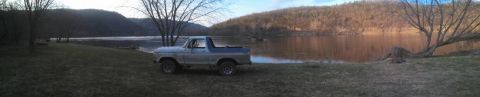 1979 Ford Bronco - A 1979 Ford Bronco is parked on a grassy bank next to a calm lake with wooded hills in the background.