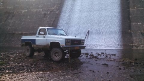 1979 Ford Bronco - GMC pickup truck parked near a waterfall.