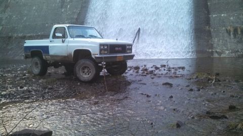 1979 Ford Bronco - A lifted GMC pickup truck is parked in a rocky, shallow stream with a waterfall in the background.
