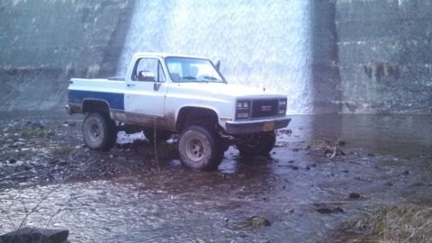 1979 Ford Bronco - A white GMC pickup truck with a blue stripe is parked in shallow water near a waterfall.