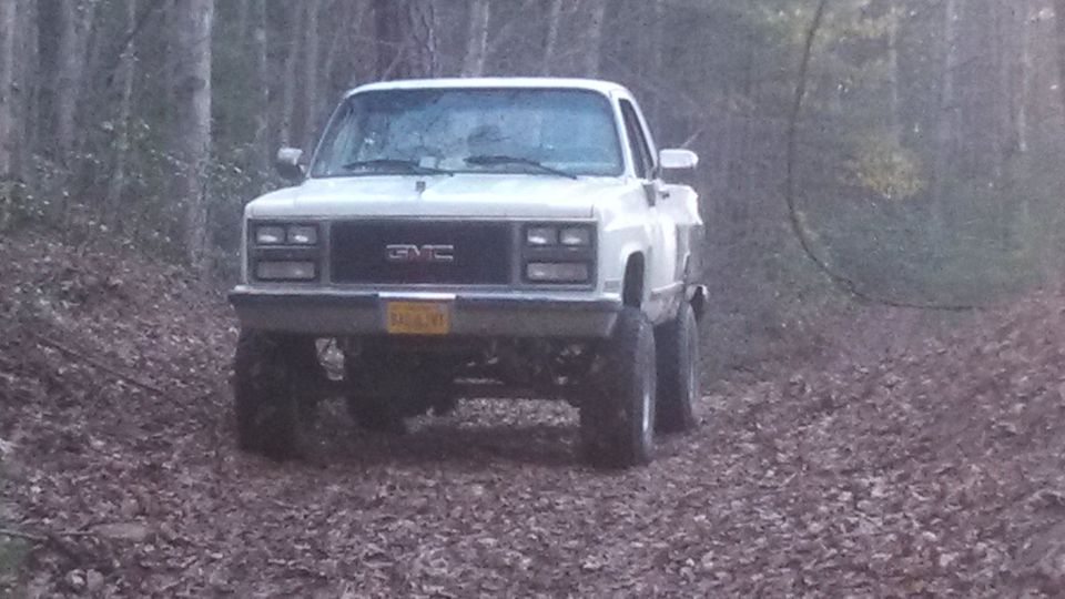 White GMC pickup truck with lifted suspension on a dirt road in a forest