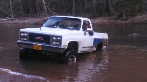1979 Ford Bronco - A white GMC pickup truck is being driven through a shallow body of water with trees in the background.