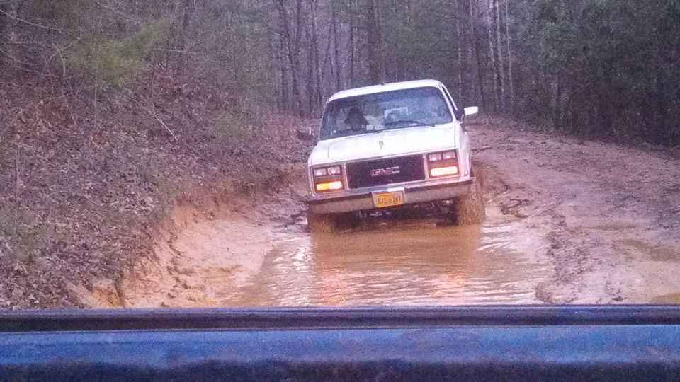 White GMC pickup truck with yellow license plate driving through a muddy trail