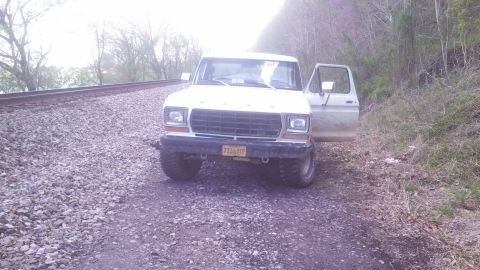 1979 Ford Bronco - A white 1979 Ford Bronco sits parked on a gravel road beside railroad tracks, with the driver's door ajar.