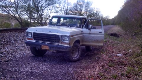 1979 Ford Bronco - Ford F-150 parked on gravel near railroad tracks, driver door ajar.