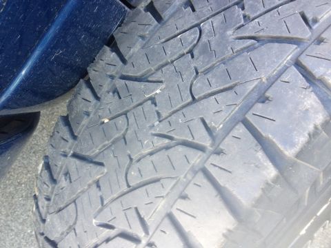 1978 Ford Bronco - A close-up view of a tire's tread pattern is shown, with a portion of a blue vehicle's body in the background.