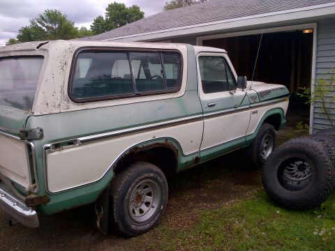 1978 Ford Bronco - A two-tone green and white 1978 Ford Bronco is seen from the side, parked in a grassy area next to a garage.
