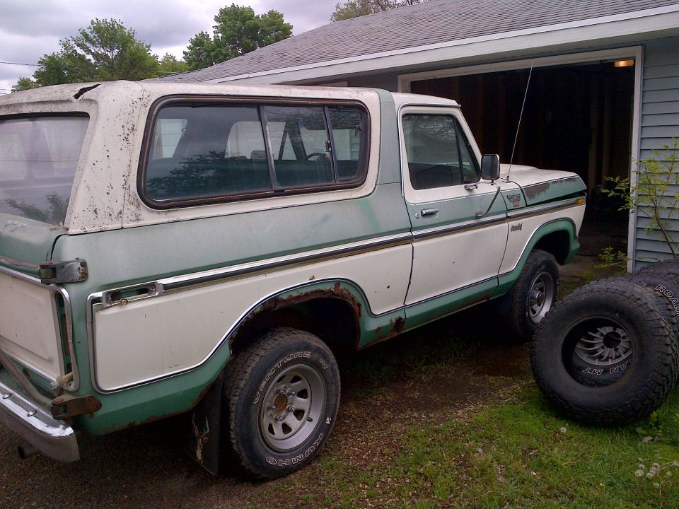 1978 Ford Bronco, two-tone green and white, showing rust and wear, parked next to a garage