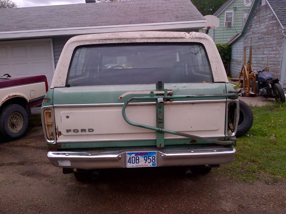 Rear view of a 1978 Ford Bronco in green and white with a bike rack and spare tire