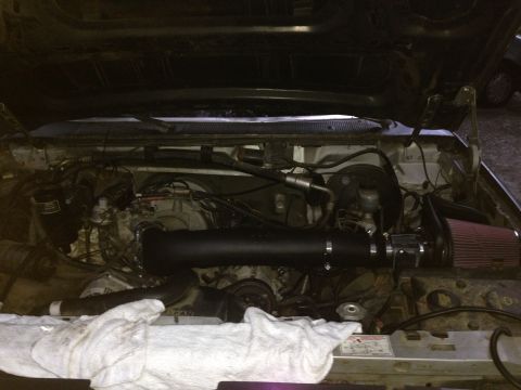 1988 Ford Bronco - The engine bay of a vehicle, an aftermarket intake system with a red air filter.