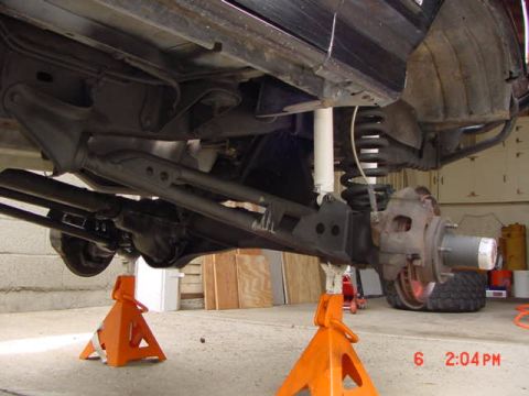 1992 Ford Bronco - The underside of a vehicle is shown, with suspension and axle parts visible while it is supported by jack stands.