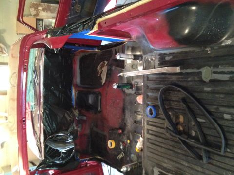 1978 Ford Bronco - The interior of a vehicle is being worked on, with red paint visible and parts covered in black plastic.
