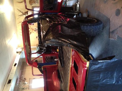 1978 Ford Bronco - A red SUV, possibly a 1978 Ford Bronco, is covered in black plastic while undergoing work indoors.