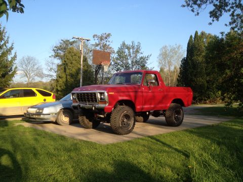 1978 Ford Bronco - A red pickup truck with a lifted suspension and off-road tires is parked next to other vehicles on a sunny day.