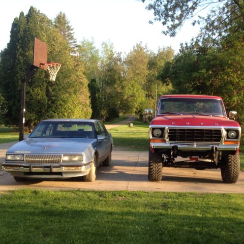 1978 Ford Bronco - A red 1978 Ford pickup truck and a blue sedan are parked outside on a sunny day.