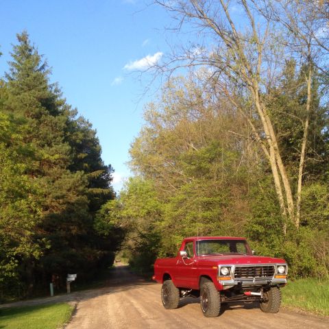 1978 Ford Bronco - A red 1978 Ford F-150 pickup truck is parked on a dirt road surrounded by trees.