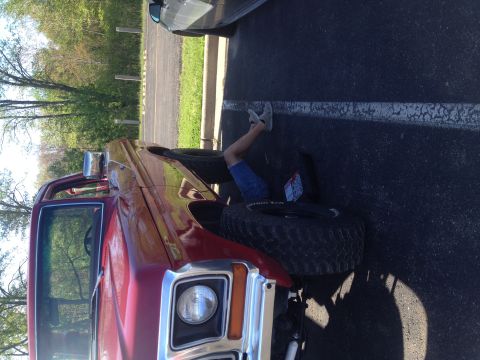 1978 Ford Bronco - Person working on the front wheel of a red 1978 Ford Bronco parked in a lot.