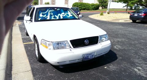 2000 Mercury Grand Marquis - A white 2000 Mercury Grand Marquis is parked, with a sunshade in the windshield.