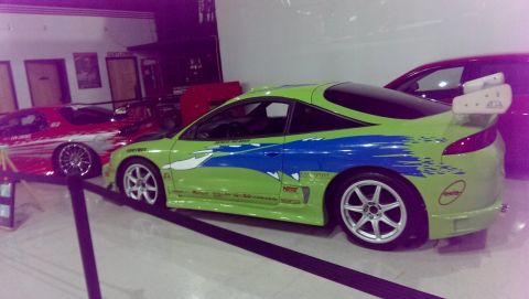 2000 Mercury Grand Marquis - A lime green sports car with distinctive blue racing stripes and a prominent rear spoiler is displayed indoors next to a red vehicle.