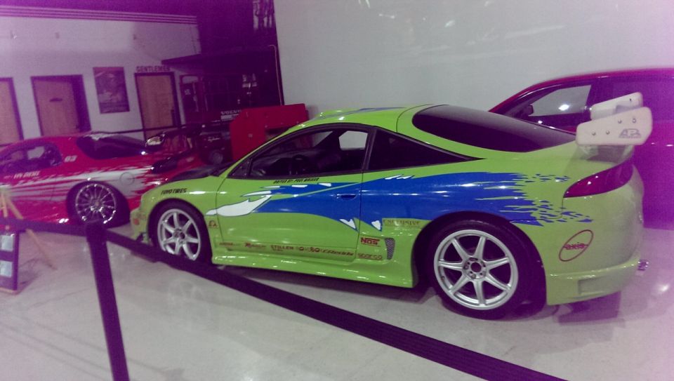 Lime green sports car with blue stripes and a large rear spoiler, parked next to a red car