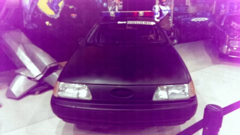 2000 Mercury Grand Marquis - A police car with a light bar is parked indoors, with other vehicles and displays in the background.