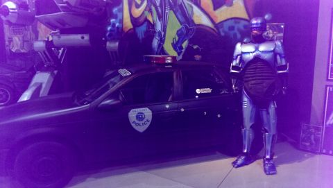 2000 Mercury Grand Marquis - A police car, possibly a 2000 Mercury Grand Marquis, is displayed with a Robocop costume and graffiti art.