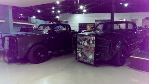 2000 Mercury Grand Marquis - Two custom pickup trucks are displayed indoors, one a collage of stickers and text on its front fender.