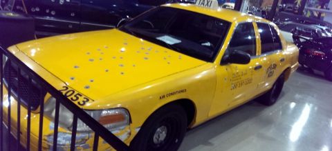 2000 Mercury Grand Marquis - A yellow taxi cab, marked with number 2053, displays extensive damage from bullet impacts on its exterior.
