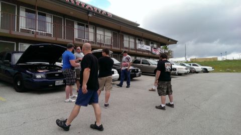2000 Mercury Grand Marquis - A group of people inspect a dark sedan with its hood open at an outdoor gathering.