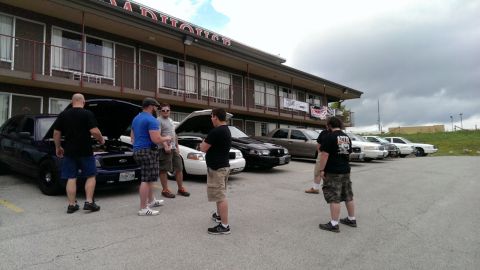 2000 Mercury Grand Marquis - Several Ford Crown Victorias are parked outside a motel, with people gathered around one of the vehicles.