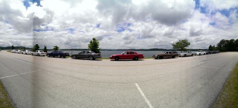 2000 Mercury Grand Marquis - Several cars are parked in a row along the edge of a body of water on a partly cloudy day.