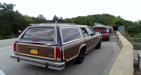 2000 Mercury Grand Marquis - A wood-paneled station wagon is seen from the rear, parked behind other vehicles on a road.
