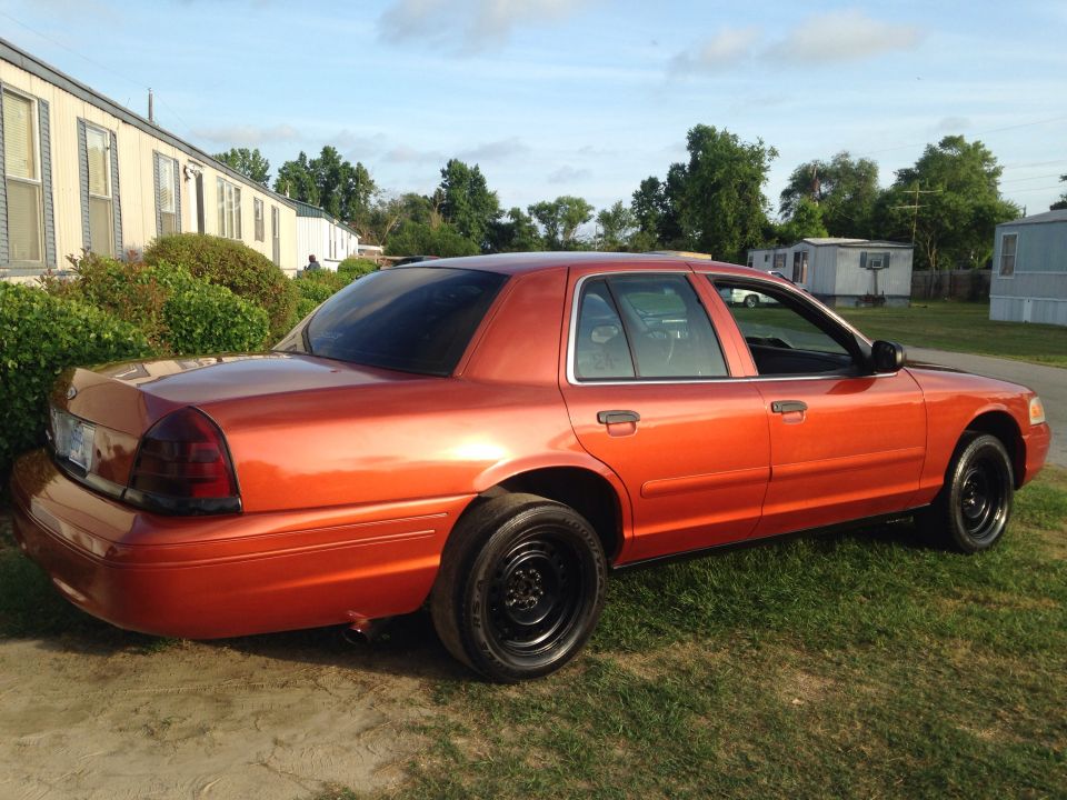 Burnt-orange Ford Crown Victoria sedan with black steel wheels parked on grass