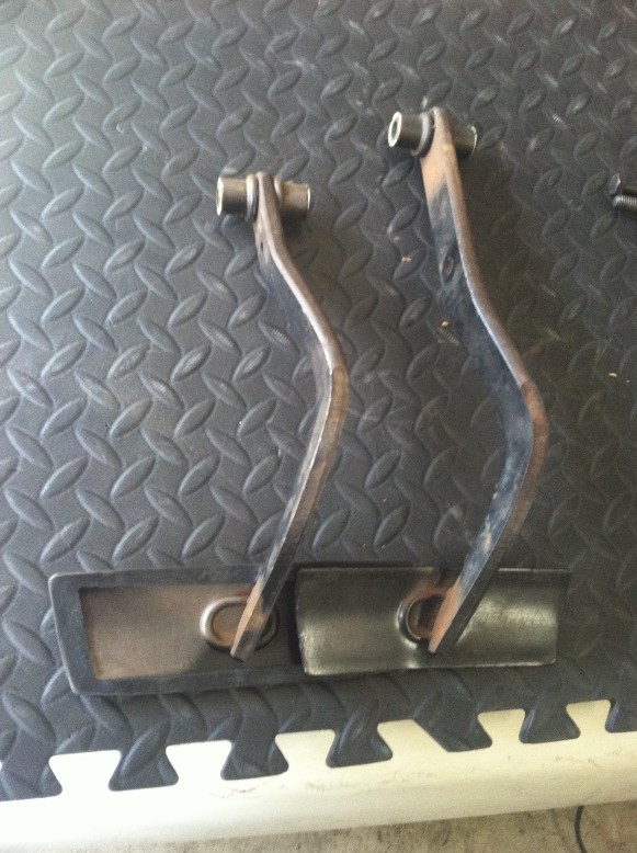 Two rusty brake pedals on a black mat. One pedal is slightly longer than the other