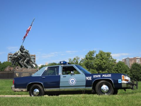 1991 Ford LTD Crown Victoria - Side profile of a blue State Police sedan marked 90E parked on grass before the Iwo Jima War Memorial.