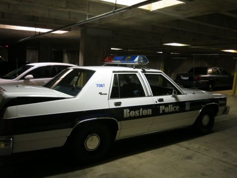 1991 Ford LTD Crown Victoria - black and white Boston Police sedan with a roof lightbar and unit number 7087 is parked in a concrete garage.