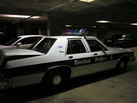 1991 Ford LTD Crown Victoria - black and white Boston Police sedan numbered 7087 with a roof lightbar sits in a dim concrete parking garage.