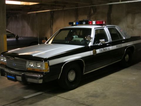 1991 Ford LTD Crown Victoria - black and white Ford sedan lettered Trumbull Police with a roof lightbar and unit 13 is parked in a concrete garage.