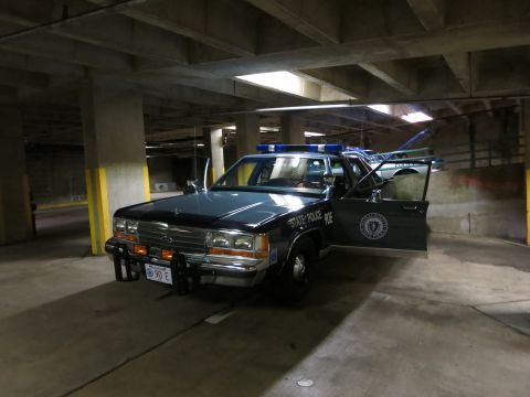 1991 Ford LTD Crown Victoria - dark State Police sedan with front push bar and roof lightbar sits with a door open inside a concrete parking garage.