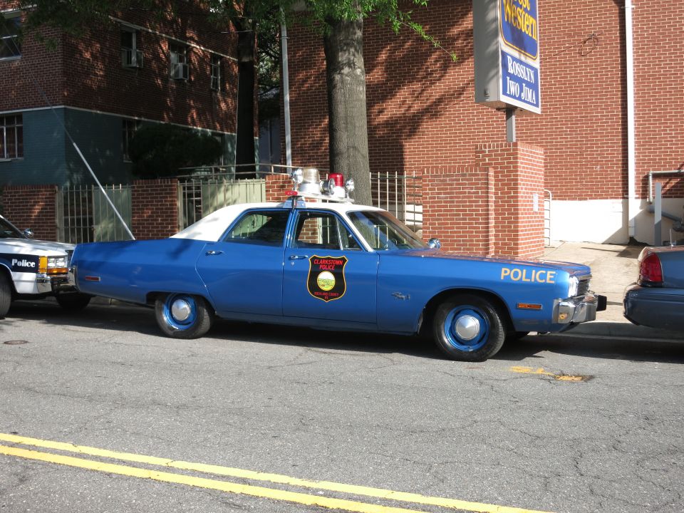 Blue and white POLICE sedan with shield emblem and roof beacons on a street