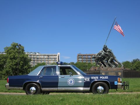 1991 Ford LTD Crown Victoria - blue-and-gray Massachusetts State Police Ford sedan, unit 90E, parked on grass beside the Iwo Jima Memorial with the U.S. flag flying.
